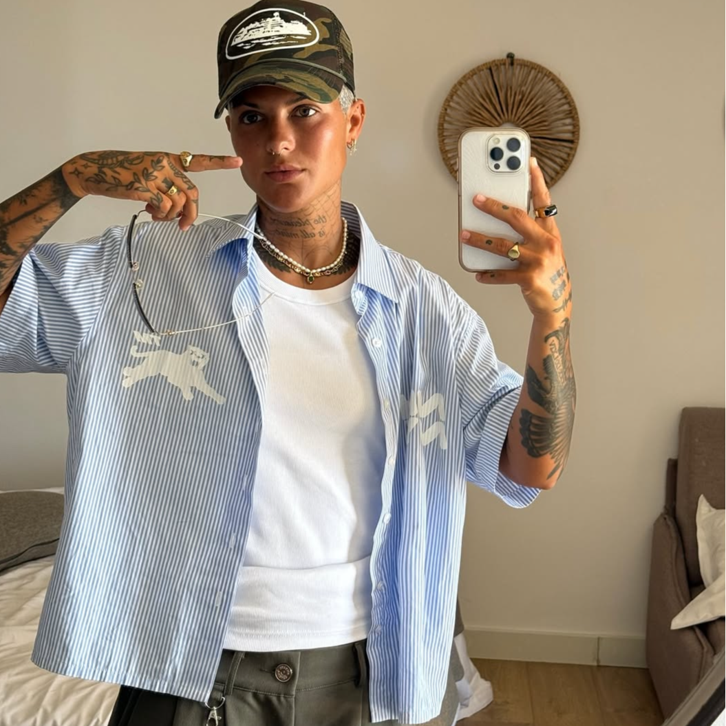 Person taking a mirror selfie wearing a classic blue NHNY Panther stripe shirt and dark cap in a room.